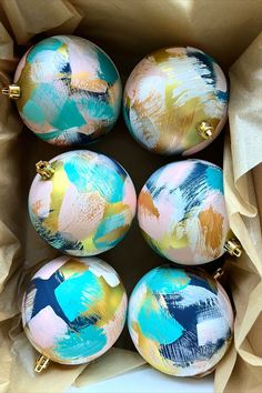 six painted ornaments are in a box on the floor with brown wrapping paper around them