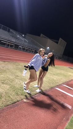 two girls are running on a track in the dark, one is holding a water bottle