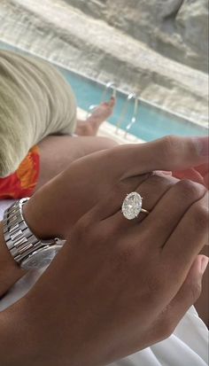 a woman laying on top of a bed next to a pool wearing a diamond ring