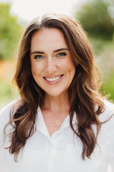 a woman with long brown hair and blue eyes smiles at the camera while wearing a white shirt