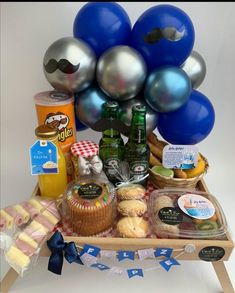 a table topped with blue balloons and other items on top of a wooden tray filled with food