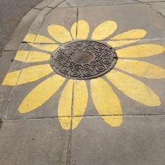 a sunflower painted on the sidewalk next to a manhole cover with an iron grate