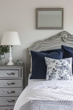 a bed with blue and white pillows in a bedroom next to a mirror on the wall