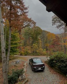 a car parked in front of a house on a gravel driveway surrounded by trees and foliage