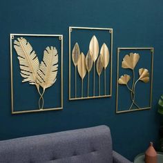 three metal wall art pieces on a blue wall next to a gray couch and green plant