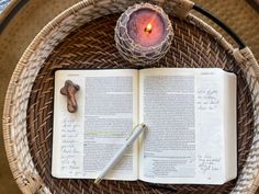 an open book on a wicker table with a lit candle and some writing utensils