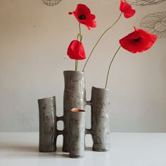 three gray vases with red flowers in them