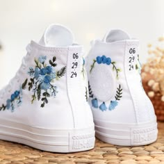 a pair of white shoes with blue flowers painted on them sitting on top of a table