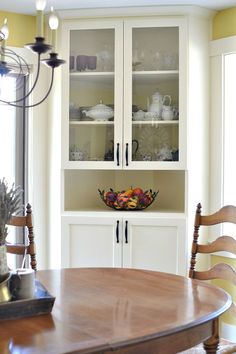 a wooden table sitting in front of a white china cabinet with glass doors on it