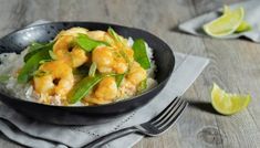 a black bowl filled with shrimp and rice on top of a wooden table next to lime wedges