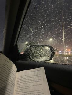 an open book sitting in the passenger seat of a car with rain falling on it