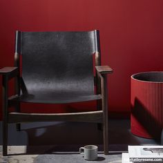 a black leather chair next to a red wall with a cup on the floor in front of it