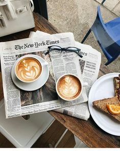 two cups of cappuccino sit on top of newspaper next to each other