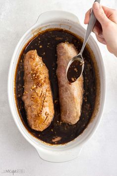 two pieces of meat in a bowl with sauce being spooned into it by someone's hand