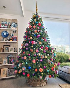 a brightly colored christmas tree in a living room next to a couch and bookcase