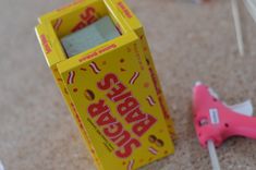 a yellow box sitting on top of a floor next to a pink pair of scissors