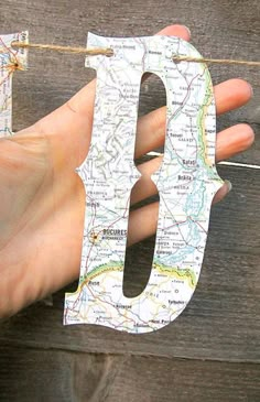 a person holding up a paper cut out of the letter d in front of a map