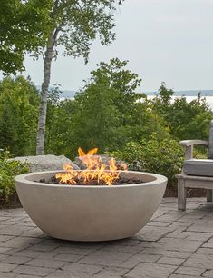 a fire pit sitting on top of a brick patio next to a chair and trees