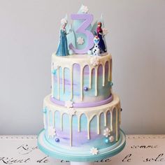 a three tiered cake decorated with frosting and frozen princess figurines on top