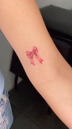 a woman's arm with a pink bow tattoo on the left side of her arm