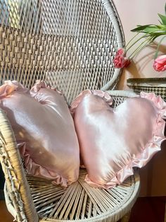 two pink pillows sitting on top of a wicker chair