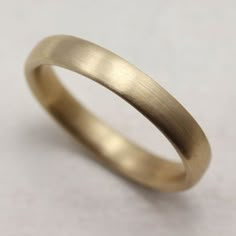 a gold wedding ring on a white surface with no one in the photo looking at it