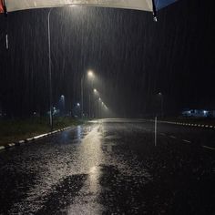 an open umbrella sitting on the side of a road at night with rain coming down