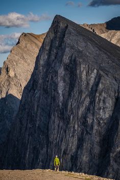 two people standing on top of a mountain next to a large rock formation with mountains in the background