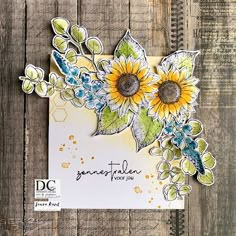 a handmade card with sunflowers and leaves on it, sitting on a wooden surface