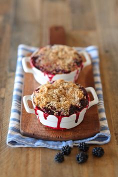 two desserts with berries and crumbled toppings sit on a wooden table