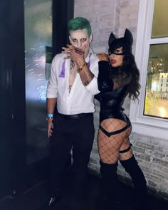 a man and woman dressed up as batman and catwoman posing for the camera in front of a brick building