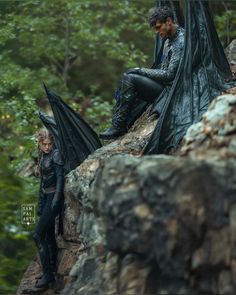 a man and woman sitting on top of a rock next to each other in the woods