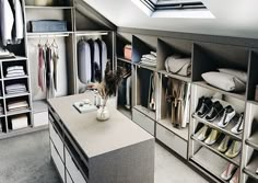 an attic closet with lots of clothes and shoes on the shelves in front of it