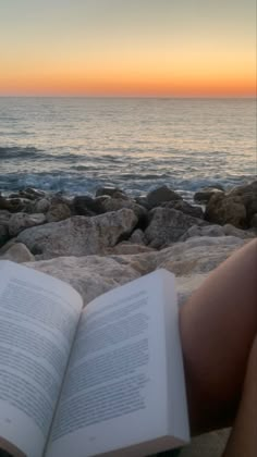 an open book sitting on top of a beach next to the ocean at sunset or sunrise