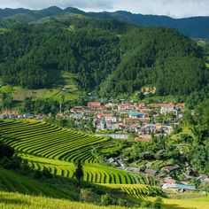 a village in the middle of a valley surrounded by lush green hills and mountains with trees on both sides