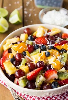 a fruit salad with kiwis, strawberries, oranges and grapes in a white bowl