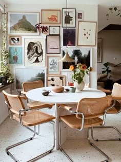 a dining room table with four chairs and pictures on the wall above it in front of a window