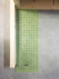 a green cutting mat sitting on top of a wooden shelf next to a white wall