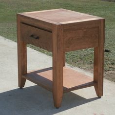 a small wooden table sitting on top of a cement ground next to grass and trees