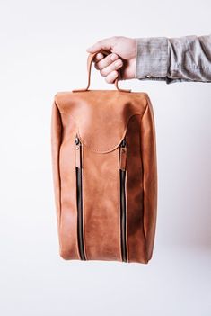 a person holding a brown leather bag with zippers on the front and side, against a white background