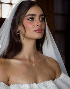 a woman in a wedding dress with a veil on her head and wearing a diamond necklace