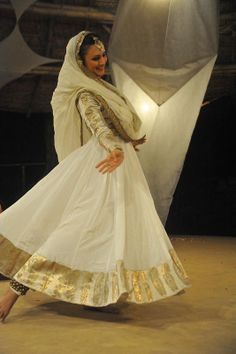 a woman in a white and gold dress is dancing with her feet on the ground