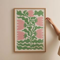 a woman is holding up a framed art piece with pink and green leaves on it