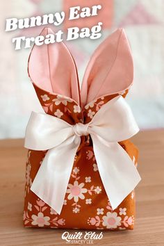 the bunny ear treat bag is decorated with pink flowers and white ribbon on an orange background