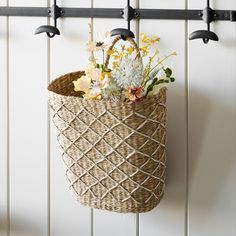 a basket hanging on the wall with flowers in it and two hooks holding them up