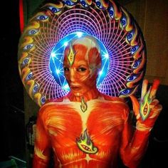 a man with painted body and head in front of a neon light circle holding his hands up