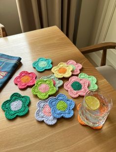 crocheted flower coasters are sitting on a table with a glass and napkin