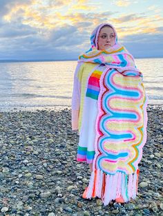 a woman standing on top of a beach covered in a colorful blanket next to the ocean