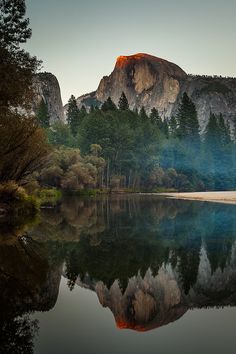 the mountains are reflected in the still water at sunset, with trees on either side