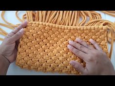 two hands are holding a yellow crochet bag with yarn on the bottom and one hand is touching it